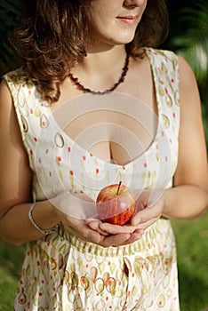 Impersonal brunette in the summer dress holding the red apple in front of her