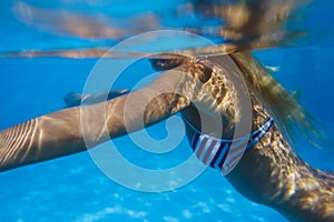 Close-up shot of a woman swimming underwater in the pool.