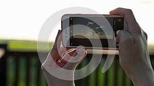 Close-up shot of woman taking pictures of sunset using smartphone.