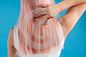 Close up shot of woman touching her smooth sleek natural long pink dyed hair while posing isolated over blue studio