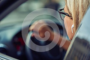 Close up shot of a woman wearing eyeglasses sitting behind steering wheel of her modern car, driving through the city