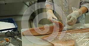 Close-up shot of a woman worker's hand in a market factory, a woman stands on the process of cutting a salmon and