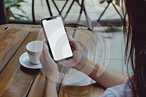 A close up shot of a woman& x27;s hand holding an phone with a blank screen sitting at an outdoor cafe table, notebook on