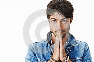 Close-up shot of worried good-looking mature guy with beard and blue eyes feeling concerned holding hands in pray over