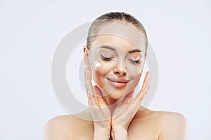 Close up shot of young adult woman with naked shoulders applies nourishing moisturising cream for soft pure skin, has tender