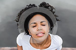 Close-up shot of young black woman smiling and closing her eyes with happy face expression, dreaming and enjoying warm summer wind