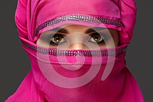 Close-up shot of a young charming woman wearing the pink hijab decorated with sequins. Arabic style.