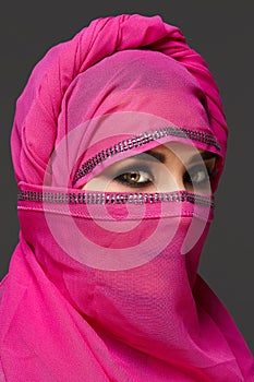 Close-up shot of a young charming woman wearing the pink hijab decorated with sequins. Arabic style.