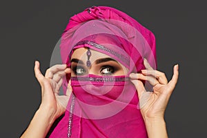 Close-up shot of a young charming woman wearing the pink hijab decorated with sequins and jewelry. Arabic style.