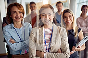 Close-up shot of a young cheerful business woman standing in the company building hallway with her colleagues and enjoys posing