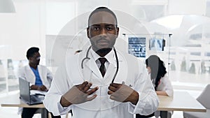 Close up shot of young male doctor putting stethoscope on the neck with team of staff on the background during