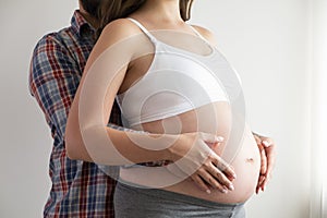 Close up shot of young man hugging his pregnant wife from behind over isolated white background. Prenatal period concept. Young