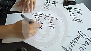 Close up shot of a young woman calligraphy writing on a paper using lettering technique. She writes Love yourself