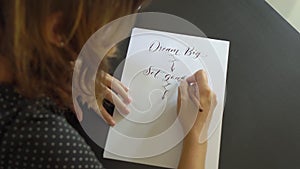 Close up shot of a young woman calligraphy writing on a paper using lettering technique. She writtes Dream big Set goals