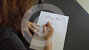 Close up shot of a young woman calligraphy writing on a paper using lettering technique. She writtes Dream big Set goals