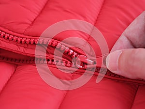 Close-up shot of a zipper on a red jacket. Hand unzipping a red jacket