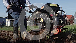 A close-up shows how a man loosens the earth using a cultivator.