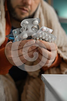 Close-up of sick man hands hold pack of different tablet blisters at home. Panacea, life save, prescribe medicament