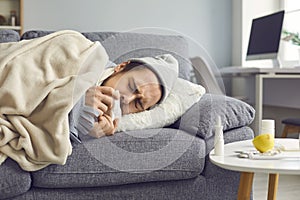 Close up of a sick man with a runny nose with a napkin in his hands lying on the couch.