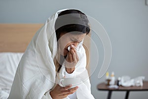 Close up sick woman wrapped into warm duvet blowing nose