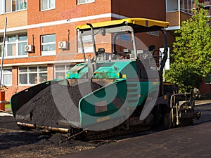 Close-up side front view of an road paver in the process of paving asphalt.