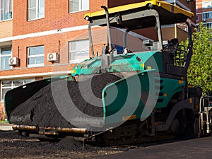 Close-up side front view of an road paver in the process of paving asphalt.