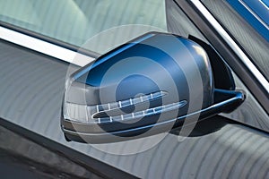 Close-up of the side left mirror with turn signal repeater and window of the car body black SUV on the street parking after