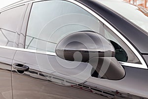 Close-up of the side left mirror and window of the car body black SUV on the street parking after washing and detailing in auto