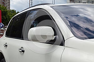 Close-up of the side left mirror with window of the car body white SUV on the street parking after washing and detailing in auto