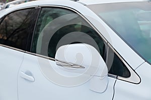 Close-up of the side left mirror and window of the car body white SUV on the street parking after washing and detailing in auto