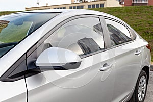 Close-up of the side right mirror and window of the car body silver sedan on the street parking after washing and detailing in