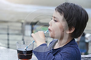Close up side view of Cute kid drinking cold drink in coffee shop by the sea, Little boy drinking soda with straw. Child drinking