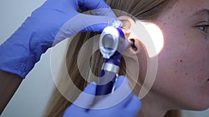 Close-up side view ear of female teenage patient with rack focus to otoscope in doctor hand. Unrecognizable