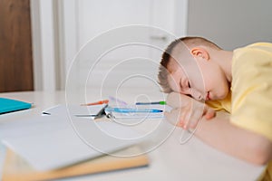 Close up side view of exhausted pupil boy sitting at home or classroom lying on desk filled with books training material