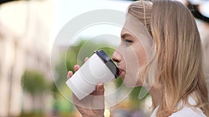Close-up side view face of pretty serious young female tourist drinking takeaway coffee and looking away sitting on city