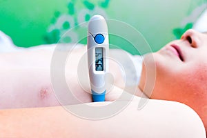 Close up side view flu sick lying down schoolboy with medical thermometer in armpit health illness