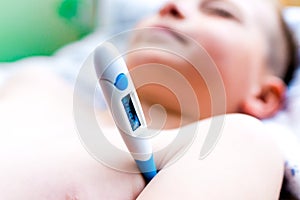 Close up side view flu sick lying down schoolboy with medical thermometer in armpit health illness