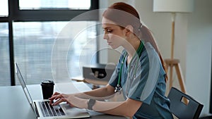 Close-up side view of focused female physician giving distant online consultation to patient via laptop computer sitting