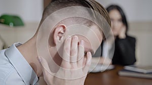 Close-up side view of frustrated male patient talking to blurred psychologist. Headshot of desperate depressed Caucasian