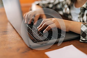 Close-up side view hands of unrecognizable elementary child school girl typing on laptop keyboard sitting at desk at