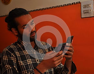 Close-up side view of a handsome bearded man with hair bun, holding two phones - Stock Photo