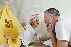 Close-up side view of a happy little girl applying paint brush to her father& x27;s face. A handsome smiling male father