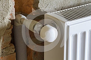 Close-up side view of isolated installed heating radiator on brick rough plastered wall in an empty room of a newly built