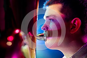 Close up side view photo of talented man, artistic musician seated, playing trumpet with soft blue-pink stage lights.