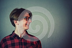 Close up side view portrait of positive boy adolescent wearing red shirt and eyeglasses looking cheerful aside isolated on gray