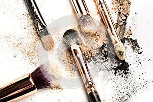 Close-up side view of professional make-up brush with natural bristle and black ferrule with crashed eyeshadow on white