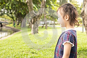 Close up and side view shot of adorable three years old asian girl standing alone in the green park outside shows lonely feeling