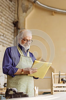 Close-up side view shot of elderly man holding exercise book in his workroom