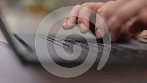 Close-up side view to unrecognizable male hands of young manager typing text on notebook keyboard outdoor. Closeup of