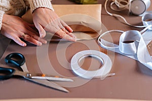 Close-up side view of unrecognizable young woman wrapping festive Christmas gift box in craft paper with presents for